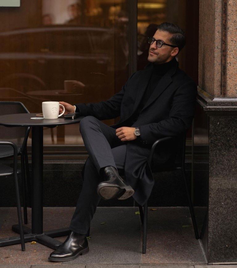 Kosta Williams with black leather chelsea boots and an all-black old money style men's outfit